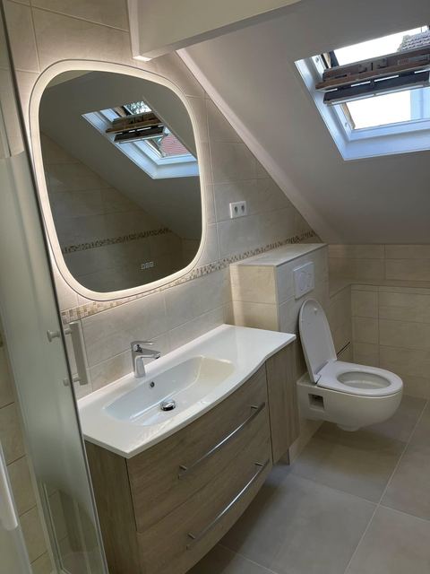 Salle de bain sous combles : meuble vasque, miroir lumineux, WC suspendu