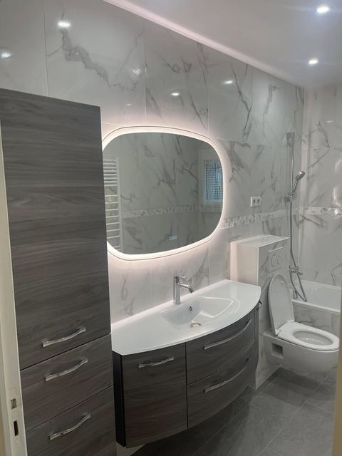 La même salle de bain refaite : murs effet marbre, meuble vasque suspendu, miroir lumineux